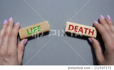 Life or Death symbol. Concept word Life or Death on wooden blocks. Businessman hand. Beautiful grey background. Business and Life or Death concept. Copy space Life or Death symbol. Concept word Life or Death on wooden blocks. Businessman hand. Beautiful grey background. Business and Life or Death concept. Copy space 112587172