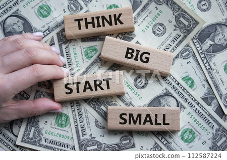 Think big start small symbol. Concept words Think big start small on wooden blocks. Beautiful dollar background. Businessman hand. Business and Think big start small concept. Copy space Think big start small symbol. Concept words Think big start small on wooden blocks. Beautiful dollar background. Businessman hand. Business and Think big start small concept. Copy space 112587224