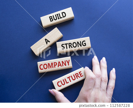 Company culture symbol. Wooden blocks with words Build a strong company culture. Beautiful deep blue background. Businessman hand. Business and Company culture concept. Copy space. Company culture symbol. Wooden blocks with words Build a strong company culture. Beautiful deep blue background. Businessman hand. Business and Company culture concept. Copy space. 112587228