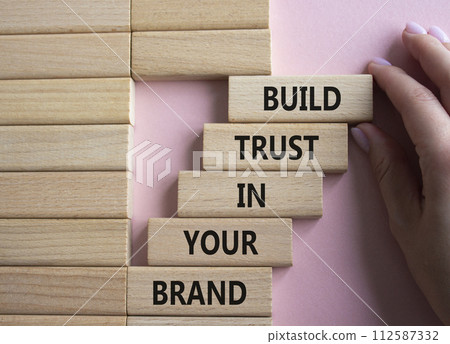 Build trust in your brand symbol. Wooden blocks with words Build trust in your brand. Beautiful pink background. Businessman hand. Business and Build trust in your brand concept. Copy space. 112587332