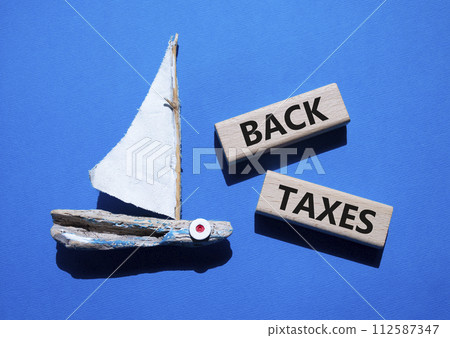 Back Taxes symbol. Concept word Back Taxes on wooden blocks. Beautiful blue background with boat. Business and Back Taxes concept. Copy space 112587347
