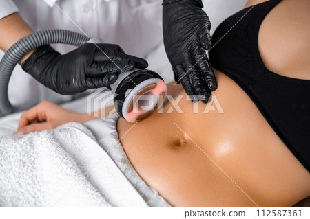 Close cosmetologist using ultrasound device while performing lifting procedure on woman belly. 112587361