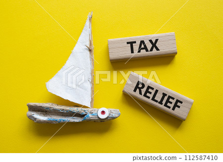 Tax Relief symbol. Concept word Tax Relief on wooden blocks. Beautiful yellow background with boat. Business and Tax Relief concept. Copy space Tax Relief symbol. Concept word Tax Relief on wooden blocks. Beautiful yellow background with boat. Business and Tax Relief concept. Copy space 112587410