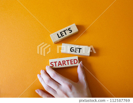 Lets get started symbol. Concept words Lets get started on wooden blocks. Beautiful orange background. Businessman hand. Business and Lets get started concept. Copy space. 112587769
