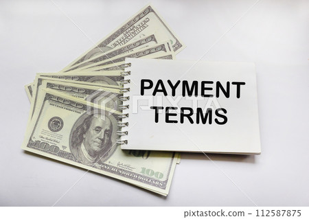 The word TERMS OF PAYMENT on a notepad with dollar banknotes on a white background The word TERMS OF PAYMENT on a notepad with dollar banknotes on a white background 112587875