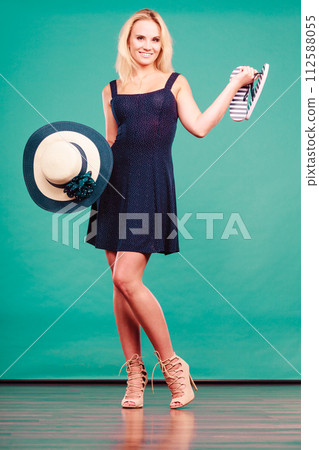 Woman wearing dress holding sun hat an flip flops 112588055