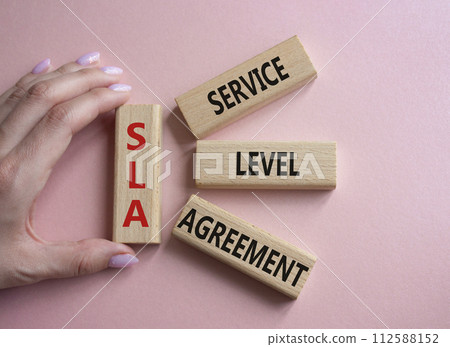SLA - Service Level Agreement. Wooden blocks with word SLA. Businessman hand. Beautiful pink background. Business and Service Level Agreement concept. Copy space. SLA - Service Level Agreement. Wooden blocks with word SLA. Businessman hand. Beautiful pink background. Business and Service Level Agreement concept. Copy space. 112588152
