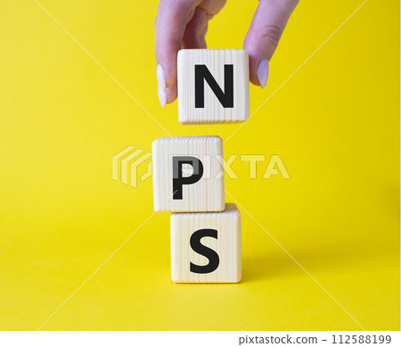 NPS - Net Promoter Score symbol. Wooden cubes with words NPS. Businessman hand. Beautiful yellow background. Business and NPS concept. Copy space. NPS - Net Promoter Score symbol. Wooden cubes with words NPS. Businessman hand. Beautiful yellow background. Business and NPS concept. Copy space. 112588199