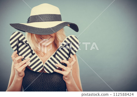 Woman wearing sun hat, holding flip flops 112588424