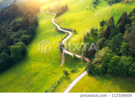 Aerial view of road in green meadows and hils at sunset in summer Aerial view of road in green meadows and hils at sunset in summer 112589009