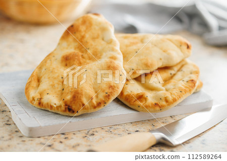 Freshly Baked Naan Bread on citting board on kitchen table. 112589264