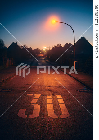 Speed Limit on street illuminated by street lamp 112589380