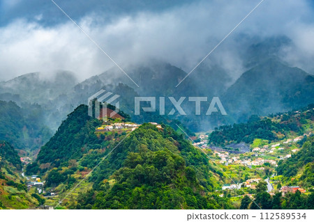 Traditional terrace village Sao Vicente, Madeira Island, Portugal. Small houses and gardens among a green mountain landscape in stormy weather. 112589534