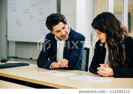 Two colleagues in an office meeting, collaborating and planning their business strategy. With documents, graphs, and smiles, their teamwork promises success. Two colleagues in an office meeting, collaborating and planning their business strategy. With documents, graphs, and smiles, their teamwork promises success. 112590332