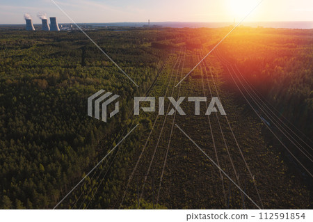 Smoking cooling towers at nuclear power plant and powerlines in forest. Sunset time. Aerial view Smoking cooling towers at nuclear power plant and powerlines in forest. Sunset time. Aerial view 112591854