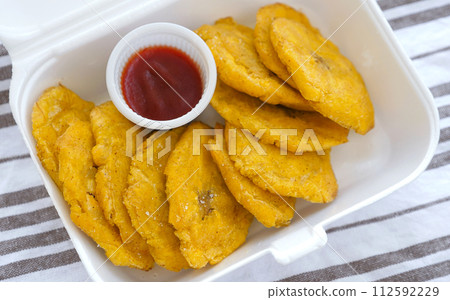 Fried platanos and sauce on plate. Sliced and cooked tostones 112592229