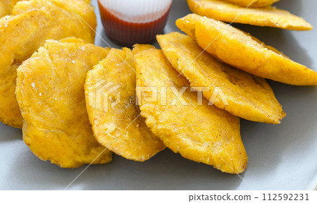 Fried platanos and sauce on plate. Sliced and cooked tostones 112592231