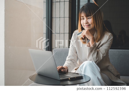 Young woman holding credit card and using laptop computer. Businesswoman working at home. Online shopping, e-commerce, internet banking, spending money, working from home concept 112592396
