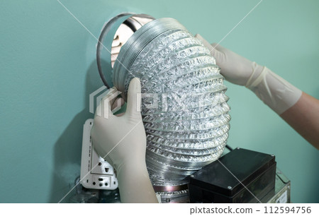 Someone trying to change an old aluminum foil of ducting pipe. Aluminium ducting is normally used where there is lots of heat like on a cooker extractor unit, because it needs to be heat resistent. 112594756