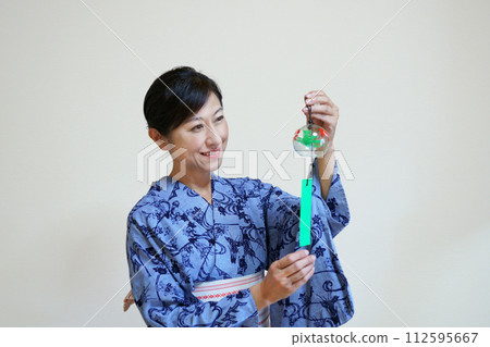 A smiling middle-aged woman wearing an indigo yukata and holding a wind chime 112595667