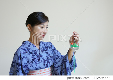 A smiling middle-aged woman wearing an indigo yukata and holding a wind chime 112595668