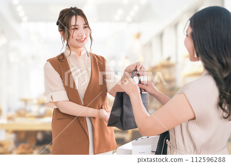 Salesperson/staff handing out paper bags to customers who shopped at a general store/apparel store 112596288