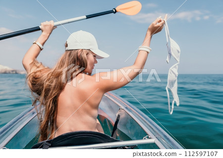 Woman in kayak back view. Happy young woman with long hair floating in transparent kayak on the crystal clear sea. Summer holiday vacation and cheerful female people relaxing having fun on the boat 112597107