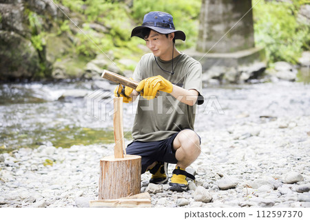 Young man chopping wood on the riverbank Battoning image 112597370