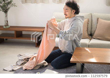 一個亞洲(日本)男人的全身,微笑在客廳裡做家務,摺衣服 一個亞洲(日本)男人的全身,微笑在客廳裡做家務,摺衣服 112597579