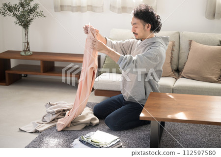 一個亞洲（日本）男人的全身，微笑在客廳裡做家務，摺衣服 112597580