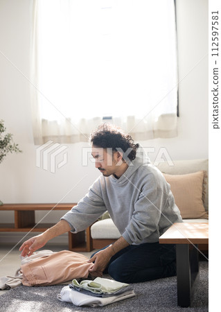 一個亞洲(日本)男人的全身,微笑在客廳裡做家務,摺衣服 一個亞洲(日本)男人的全身,微笑在客廳裡做家務,摺衣服 112597581