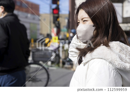 A young woman wearing a mask waiting at a railroad crossing 112599959