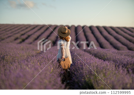 Back view woman lavender sunset. Happy woman in white dress holds lavender bouquet. Aromatherapy concept, lavender oil, photo session in lavender 112599995