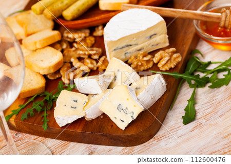 On table there is cutting board with blue cheese, honey, hardtack, walnut decorated with arugula 112600476