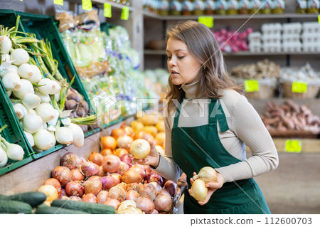 Female seller working in supermarket and lays out onions on counter Female seller working in supermarket and lays out onions on counter 112600703