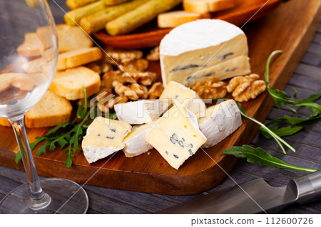 On table there is cutting board with blue cheese, hardtack and walnut decorated with arugula On table there is cutting board with blue cheese, hardtack and walnut decorated with arugula 112600726