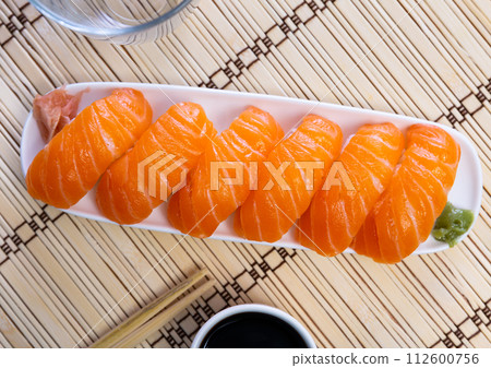 Blue rectangular ceramic plate of delicious salmon nigiri with soy souse on bamboo mat. Blue rectangular ceramic plate of delicious salmon nigiri with soy souse on bamboo mat. 112600756