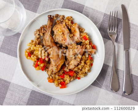 Lunch is served on plate - baked pieces of young rabbit and pearl barley 112600829