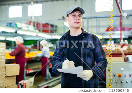 Positive male worker fills out a document at a citrus processing plant. 112600846