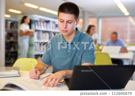 Young male student studying with a laptop in the library 112600879