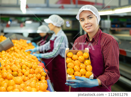Cheerful girl worker with box of tangerines at fruit sorting factory 112601276