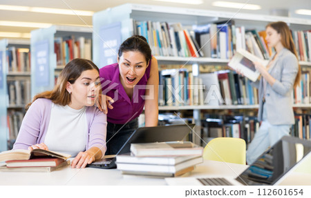 Two surprised female colleagues working on join project in library Two surprised female colleagues working on join project in library 112601654