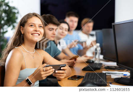 At computer class, young girl student sits with mobile phone and listens admiringly to teacher 112601655