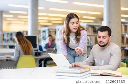 Students in the library are engaged on a laptop, discussing something 112601685