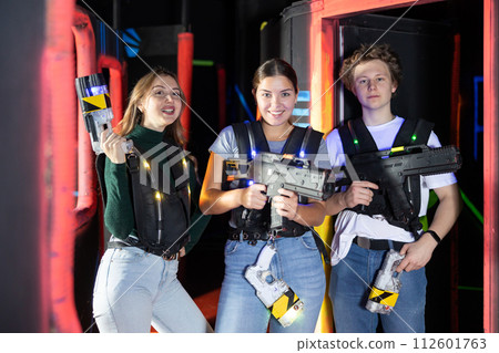 Two girls and one guy posing with lasertag guns in arena Two girls and one guy posing with lasertag guns in arena 112601763
