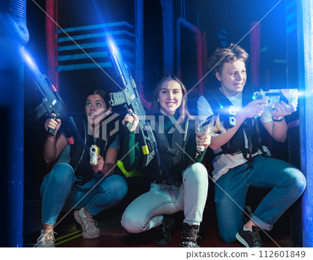 Modern young people with laser pistols playing laser tag on dark labyrinth Modern young people with laser pistols playing laser tag on dark labyrinth 112601849
