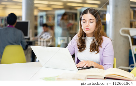 Portrait of woman with laptop and book in public library closeup Portrait of woman with laptop and book in public library closeup 112601864