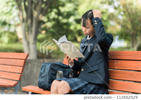 Junior high school and high school girls in uniforms sitting on a bench in the park and reading books, textbooks, and notes (difficult/troubled/thinking) 112602029