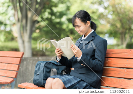 Junior high school and high school girls in uniforms sitting on a park bench and reading books, textbooks, and notebooks 112602031