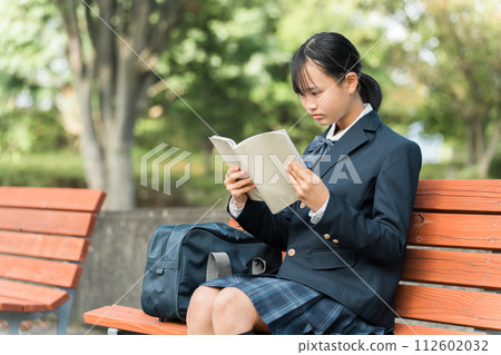 Junior high school and high school girls in uniforms sitting on a park bench and reading books, textbooks, and notebooks 112602032